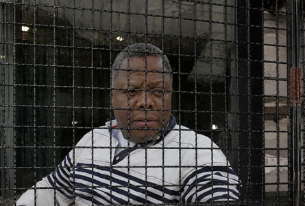 Erick Mauro Nguémah, derrière les grilles, à trois jours de la probable inauguration du monument qu'il a porté pendant trois ans. (Illustration générée par IA) © GabonReview